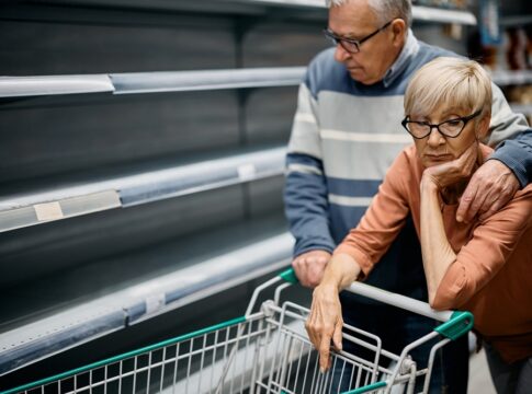 Worried elderly couple before empty supermarket shelves.