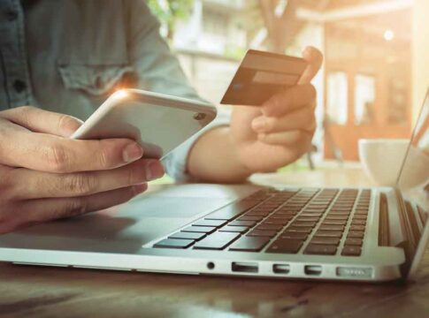 Person using credit card and smartphone near laptop.