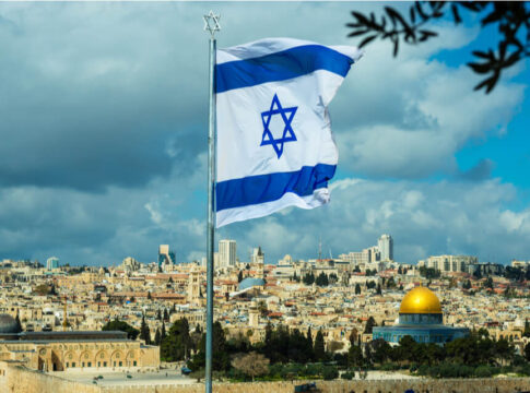 Israeli flag flying over Jerusalem skyline with Dome of Rock.