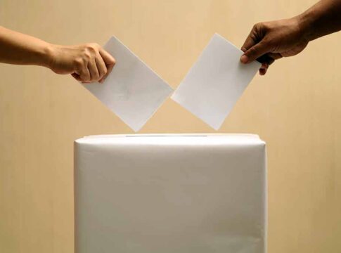 Two hands placing ballots into a voting box.