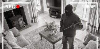 Home security footage of masked intruder with crowbar.