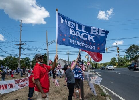 Pro-Trump supporters on street corner with 2024 flags.