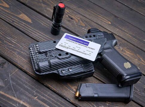 Pistol, holster, permit, flashlight, and magazine on wooden background.