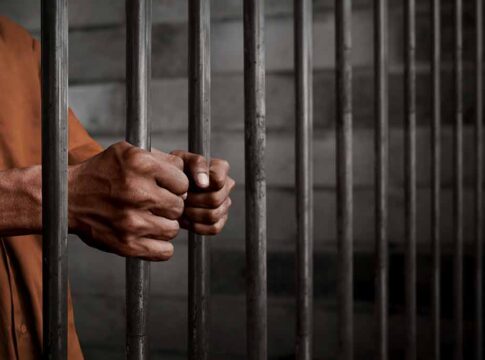 Hands gripping prison cell bars tightly.