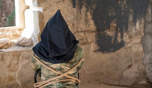 Person hooded and bound in abandoned stone room.