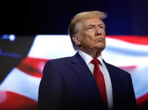 donald trump in suit with red tie American flag backdrop