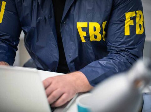 Person wearing FBI jacket working on a laptop.