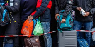 People standing with luggage behind a red and white tape.
