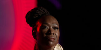 A woman speaking on stage under red lighting.