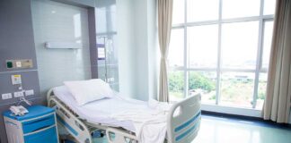 Empty hospital bed next to large window.