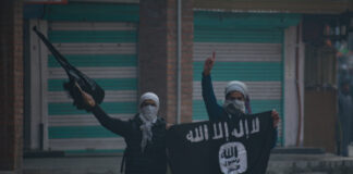 Two masked individuals holding a flag and gun.