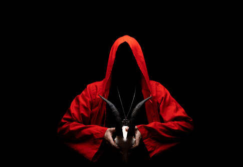 Hooded figure in red cloak holding a goat skull.