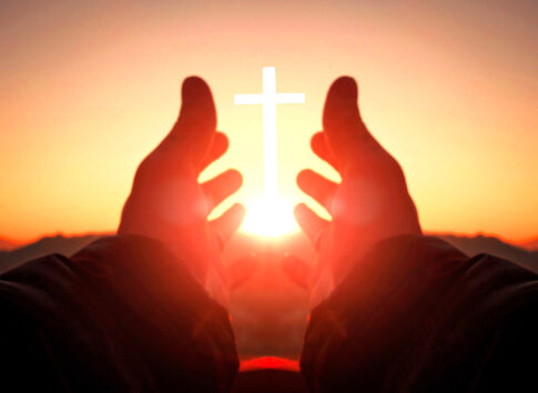 Hands reaching toward sun and cross at sunrise.