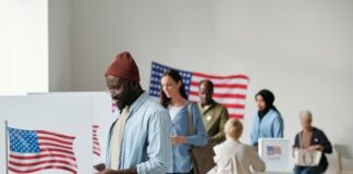 People voting at polling station with American flag nearby.