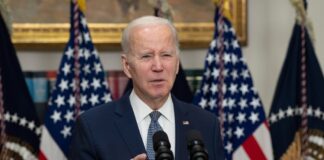Man speaking at podium with American flags behind