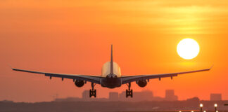 Airplane landing at sunset on illuminated runway.