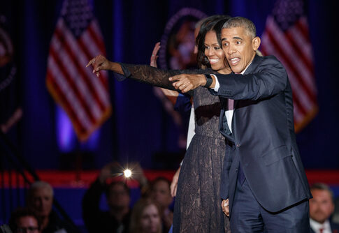 Two people onstage, smiling and pointing at something.