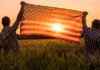 Two people hold an American flag in a field.