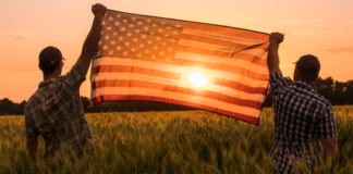 Two people hold an American flag in a field.