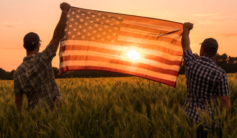 Two people hold an American flag in a field.