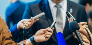 Multiple microphones held towards a person in suit.