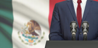 Man in suit with Mexican flag speaking at podium