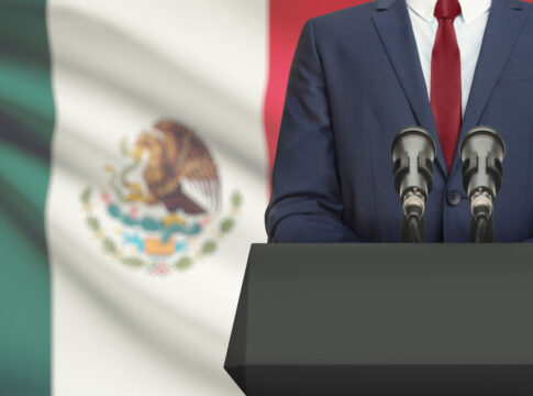 Man in suit with Mexican flag speaking at podium