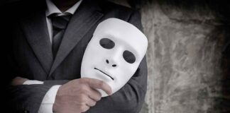 Person in suit holding a white mask.