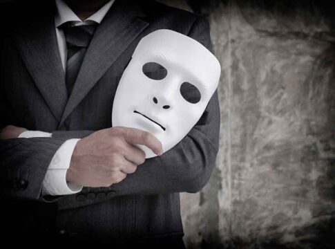 Person in suit holding a white mask.