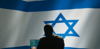 Hacker in front of Israeli flag with laptop.