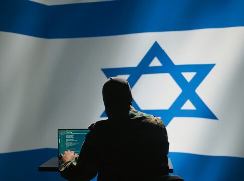 Hacker in front of Israeli flag with laptop.