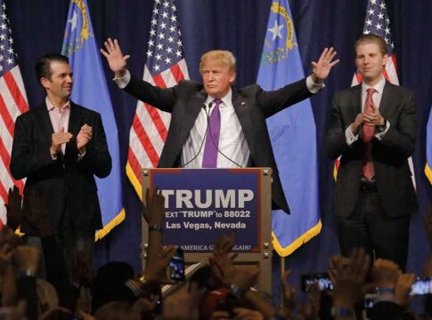 Man at podium with arms raised, flanked by applauding men.