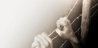 Hands gripping barbed wire fence.
