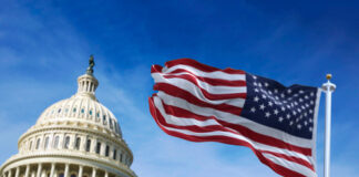 U.S. Capitol building with American flag waving in foreground.