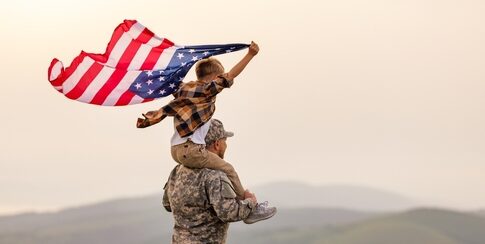Child on soldiers shoulders holding American flag.