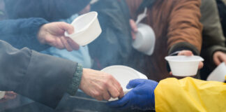 People receiving food in plastic bowls from a server.