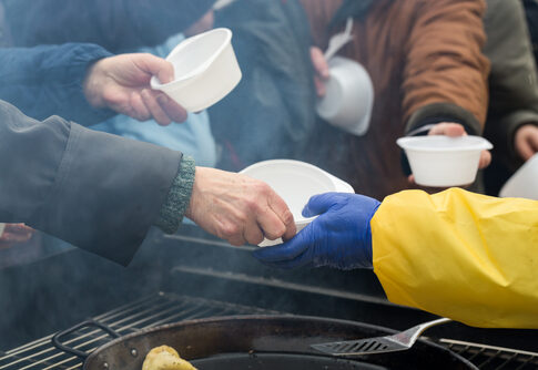 People receiving food in plastic bowls from a server.