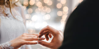 Groom placing ring on bride's finger at wedding.
