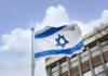 Israeli flag waving near a building with windows.
