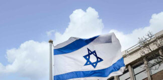 Israeli flag waving near a building with windows.