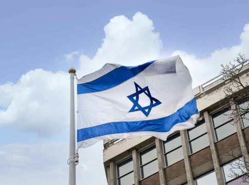 Israeli flag waving near a building with windows.