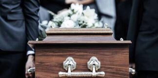 Pallbearers carrying a wooden coffin with white flowers.