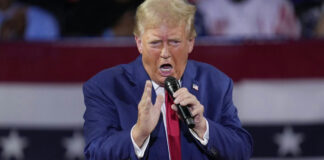 A man in a blue suit passionately speaking into a microphone at a rally