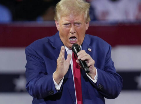 A man in a blue suit passionately speaking into a microphone at a rally