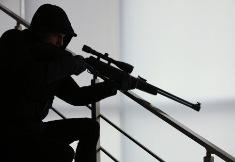 A silhouetted figure in tactical gear aiming a sniper rifle from a staircase