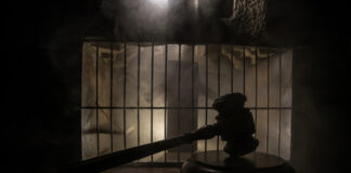 A gavel placed on a wooden surface in front of a barred cage with a smoky background