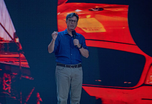 Stephen Colbert speaking on stage with a vibrant backdrop