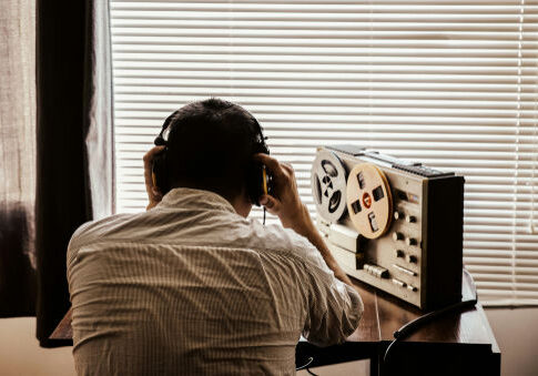 Person listening to tape recorder with headphones by window.