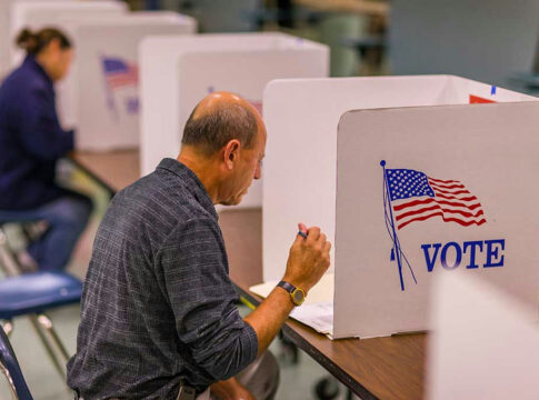 Man voting in a booth with American flag.