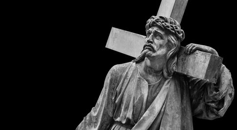 A black and white statue of Christ carrying a cross with a sorrowful expression